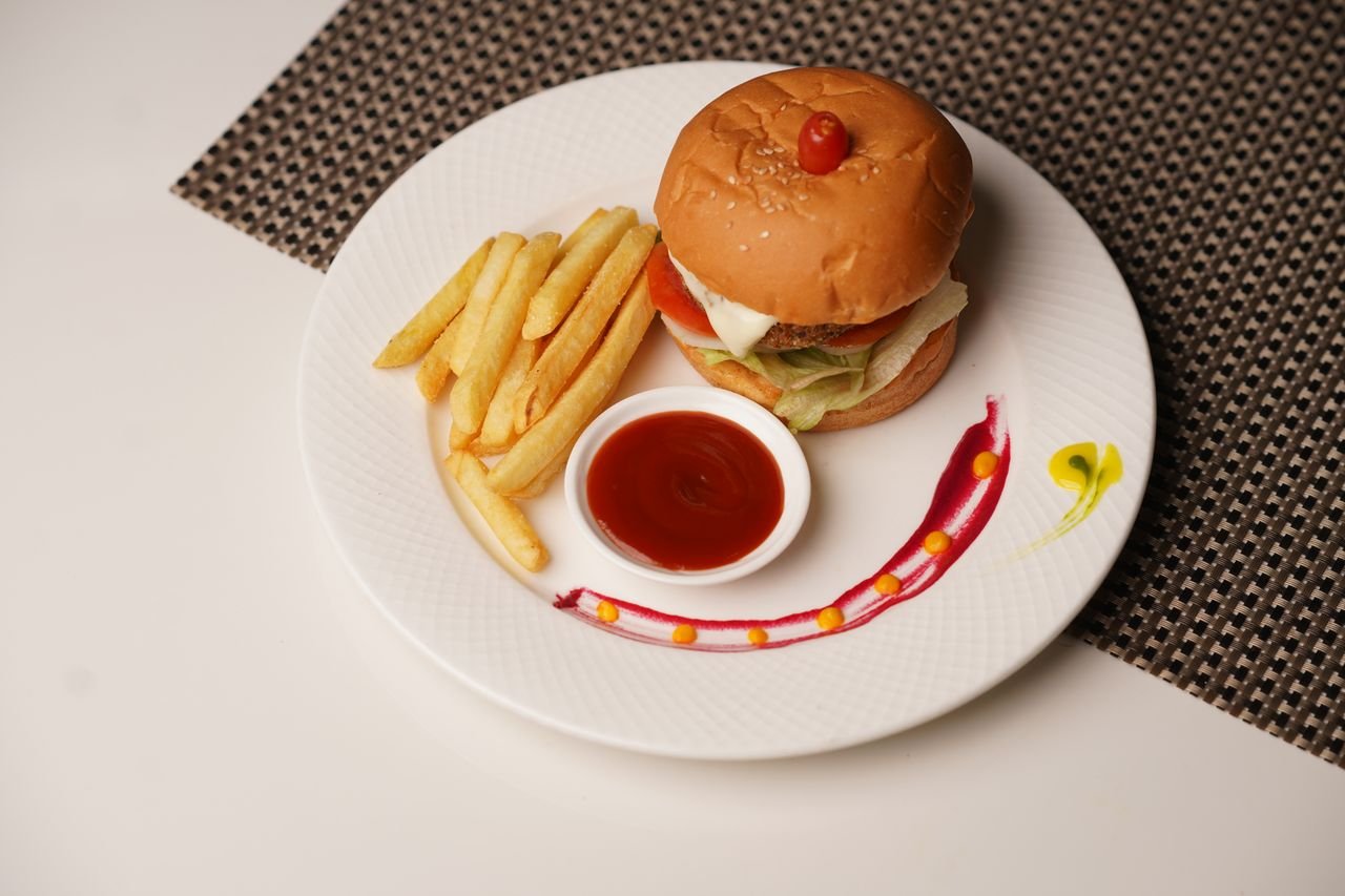 services-04 Tasty burger with fries and ketchup elegantly served on a decorated plate.
