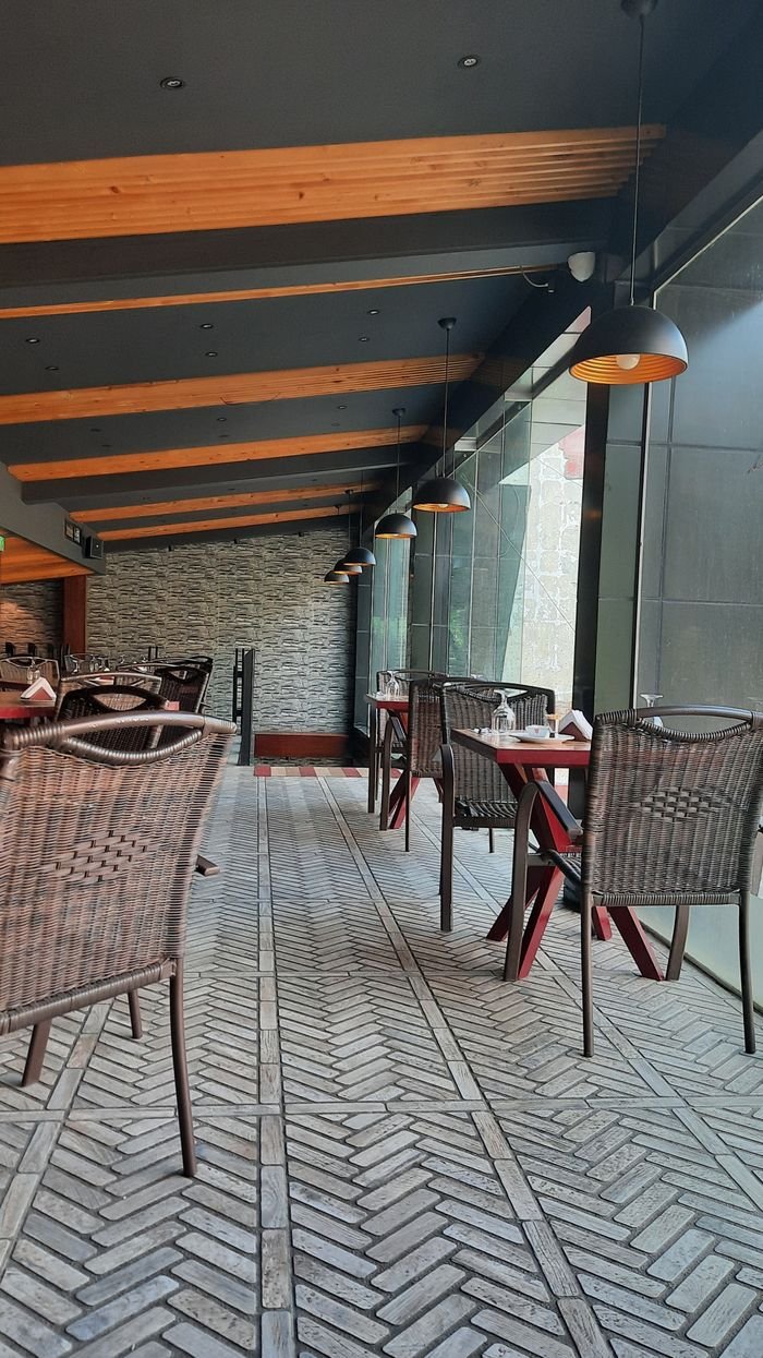 who-we-are Stylish indoor dining area featuring wicker chairs, wooden beams, and large windows for natural light.