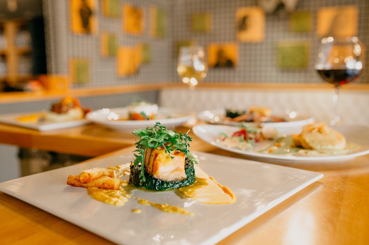 services-01 Various appetizing dishes served on white plates and glasses of wine on wooden table in modern light restaurant